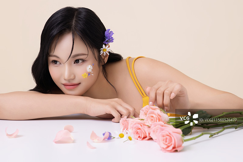 一位美丽的女性面部涂有彩绘，躺在桌子前，轻触花朵。图片素材