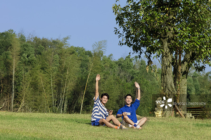 坐在草坪上打招呼的两个年轻男子图片素材