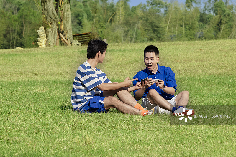坐在草坪上玩手机游戏的两个年轻男子图片素材