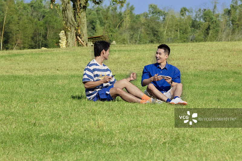 坐在草坪上玩手机游戏的两个年轻男子图片素材