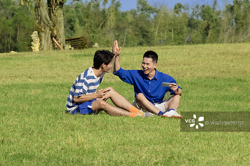 坐在草坪上击掌的两个年轻男子图片素材