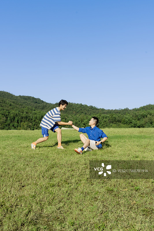 坐在草坪上玩手机游戏的两个年轻男子图片素材