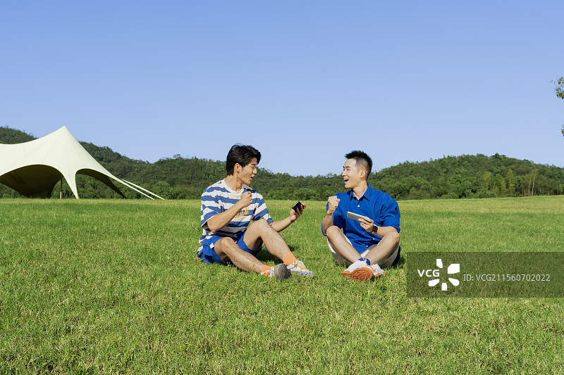 坐在草坪上玩手机游戏的两个年轻男子图片素材