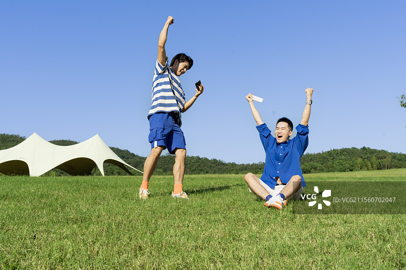 坐在草坪上玩手机游戏的两个年轻男子图片素材