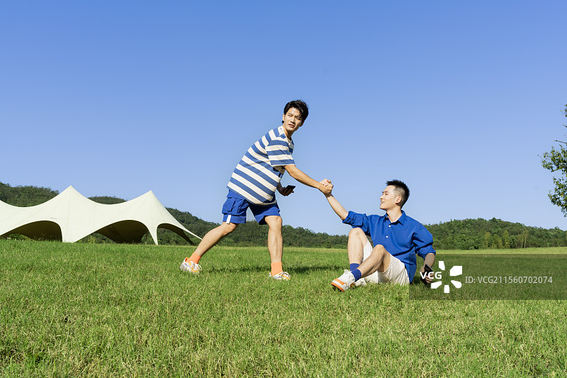 坐在草坪上玩手机游戏的两个年轻男子图片素材