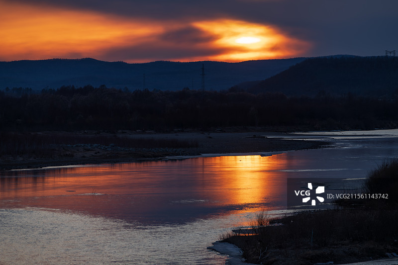 冬季四月上旬傍晚夕阳西下，大兴安岭加格达奇区冰层融化的甘河，壮丽晚霞在水面形成倒影，色彩绚烂图片素材