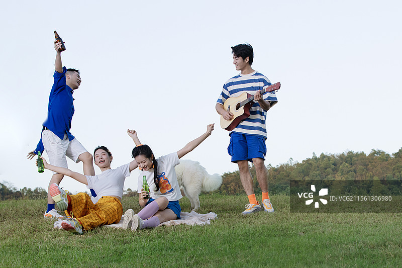 坐在草坪上喝啤酒弹吉他的四个年轻人图片素材
