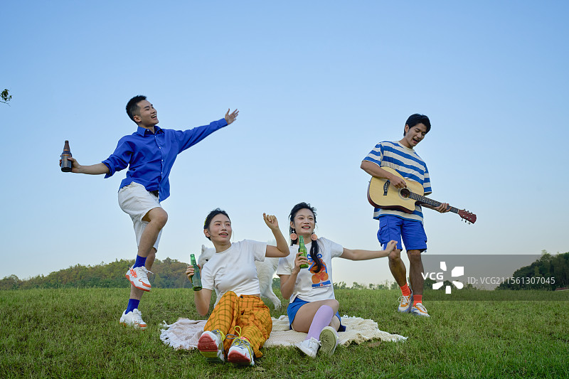 坐在草坪上喝啤酒弹吉他的四个年轻人图片素材