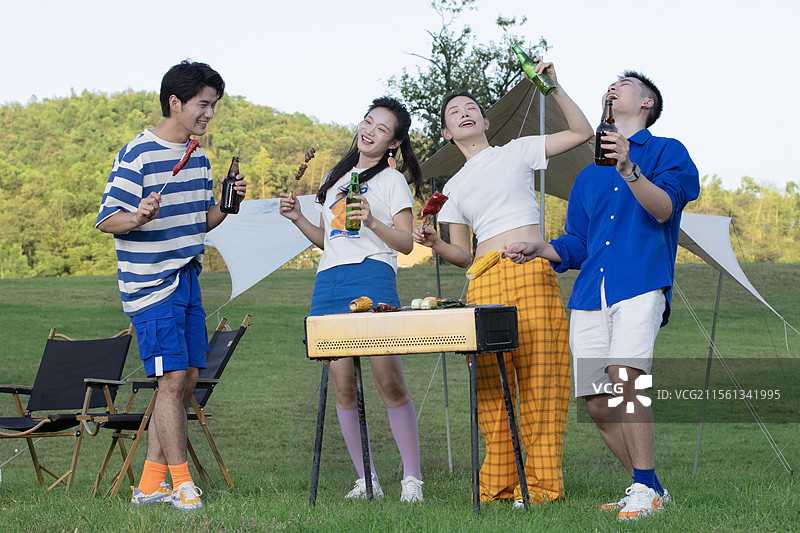 围在烧烤炉前吃烧烤的四个年轻人图片素材