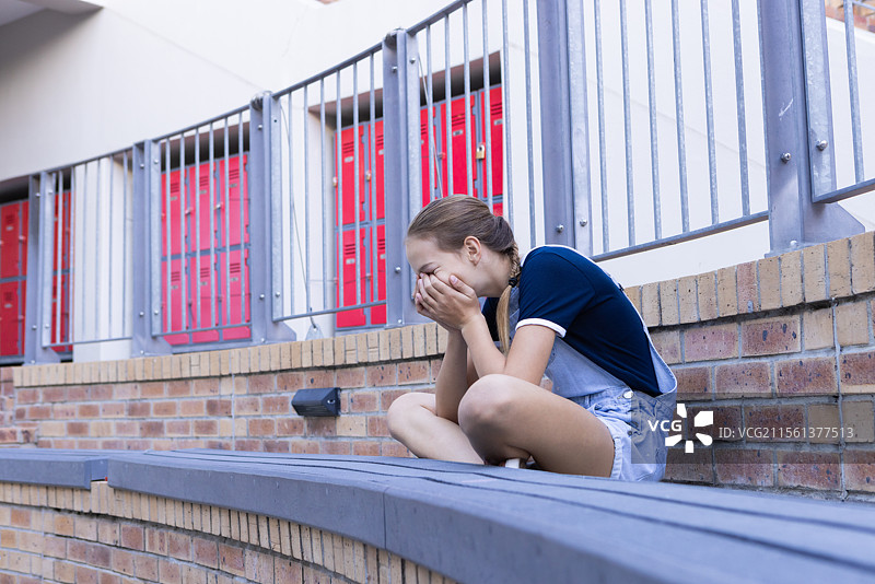 女孩在学校里独自坐着，双手捂住脸哭泣。图片素材