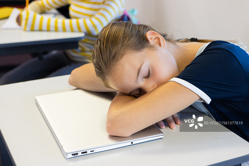 在课堂上上课时，女孩趴在桌子上睡觉，旁边有笔记本电脑。图片素材