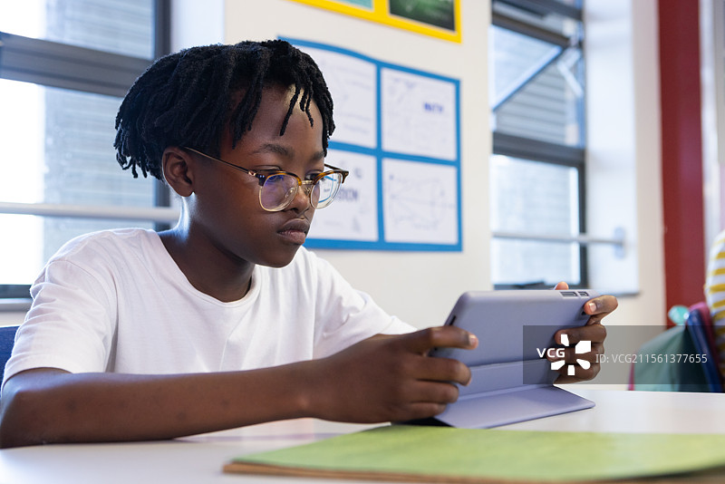 在学校，非裔美国男孩在桌子上使用平板电脑，专注于数字学习图片素材