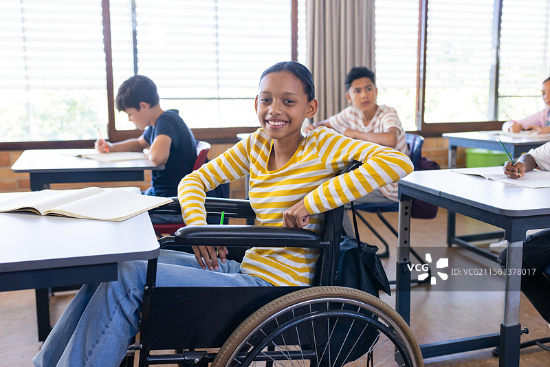 在学校，坐在轮椅上的女孩微笑着与同学们一起在教室学习图片素材