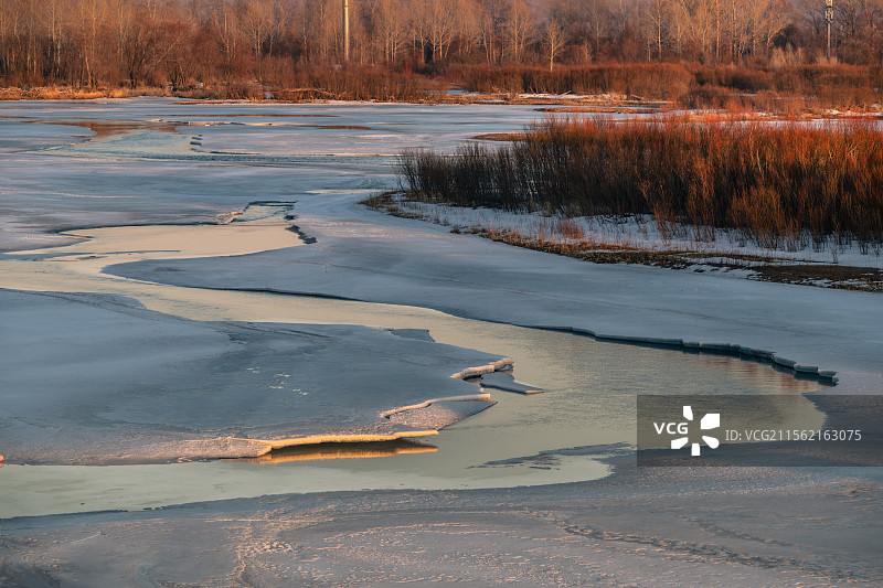 四月上旬大兴安岭加格达奇区甘河，冰封的河流逐渐开冻，露出河水S型流淌，夕阳照在冰层和沙洲树林上图片素材