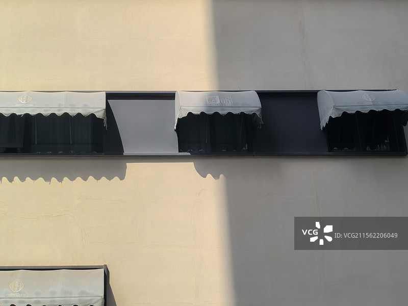 一面黄墙灰窗上都装有遮阳棚，一半沐浴在阳光下，一半被楼阴遮挡图片素材