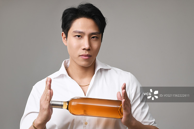 灰色背景下拿着酒瓶的年轻人的肖像图片素材