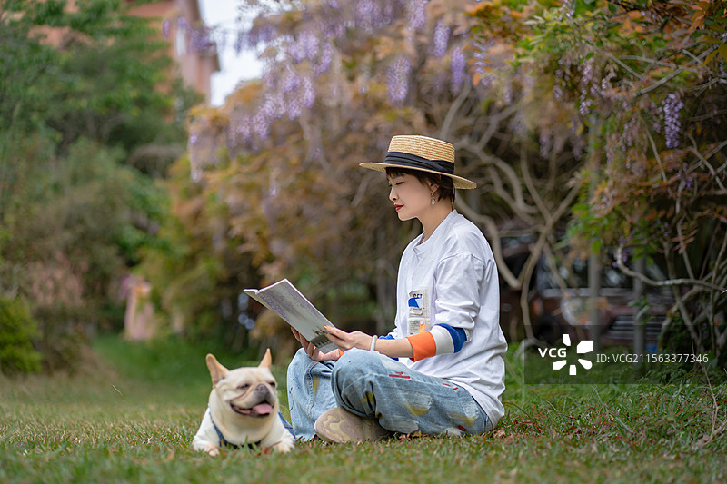 草地上看书的东方美女与宠物狗斗牛犬图片素材