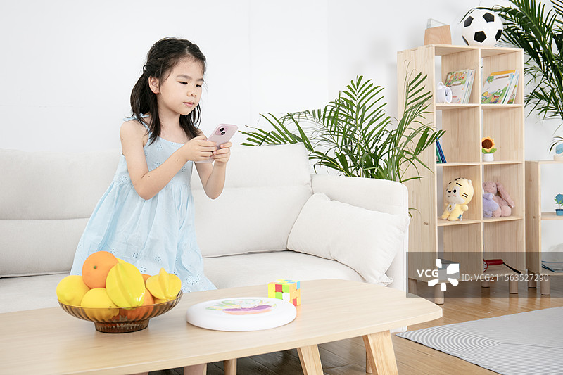 穿蓝色吊带裙的小女孩玩手机图片素材