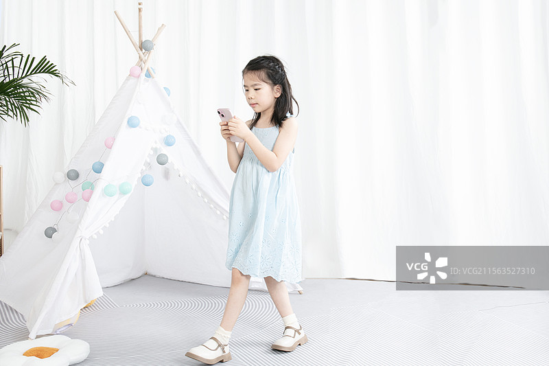 穿蓝色吊带裙的小女孩玩手机图片素材