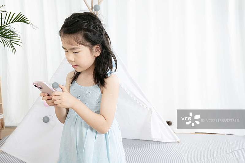 穿蓝色吊带裙的小女孩玩手机图片素材