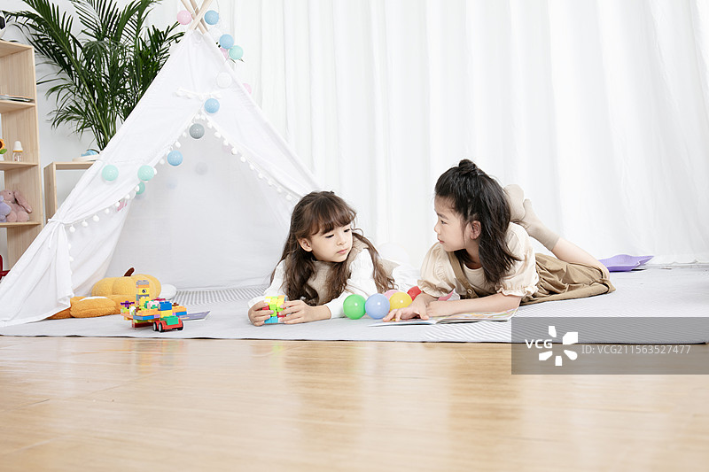 趴在地毯上看书玩耍的两个小女孩图片素材