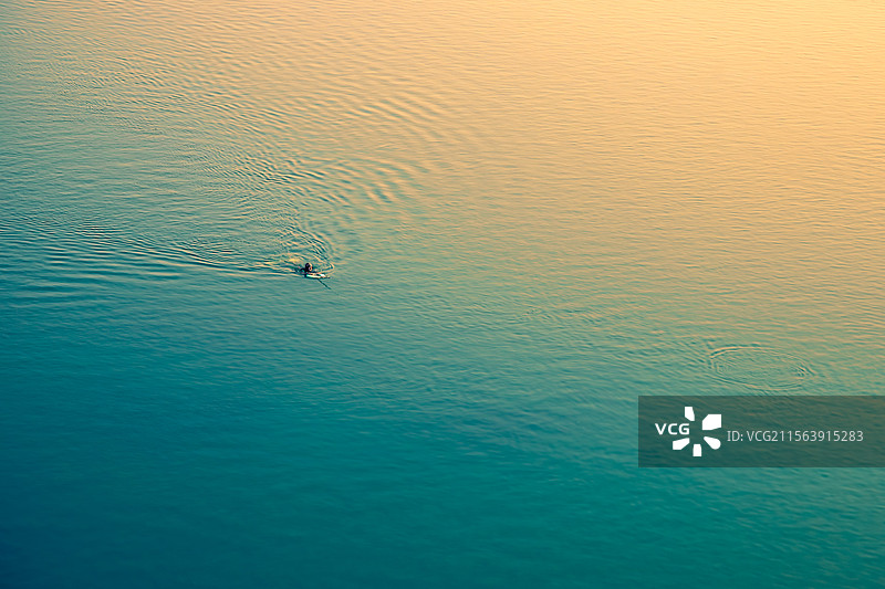夕阳下浮在平静水面上的鱼叉捕鱼者图片素材