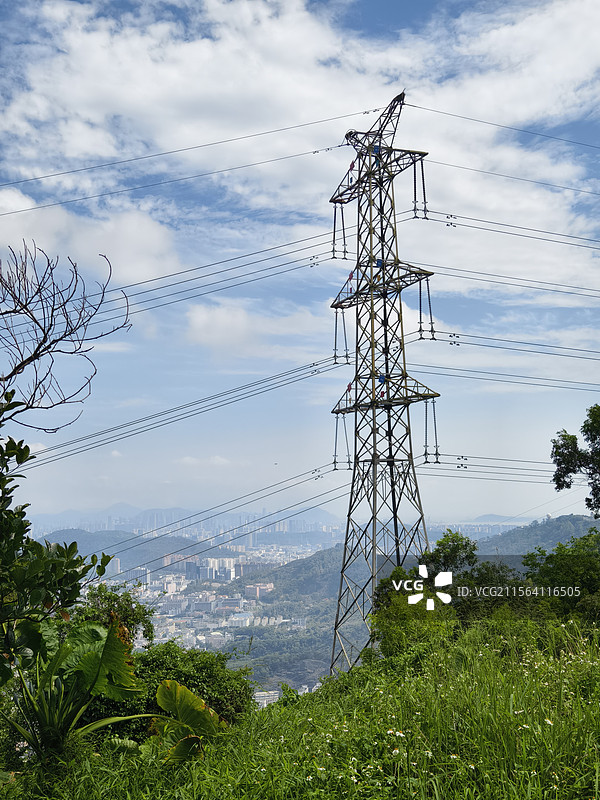 高耸输电铁塔于绿野间挺立，电线纵横，蓝天白云下城市远景朦胧，展自然与电力景观图片素材