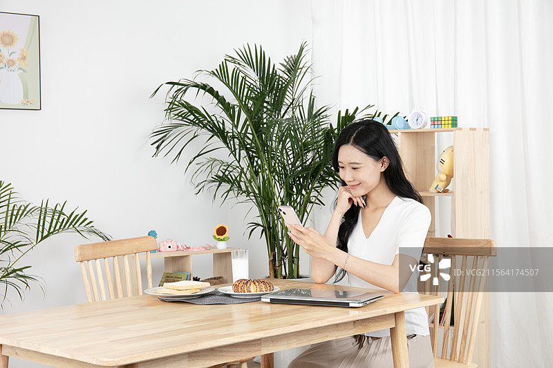 边吃早餐边刷手机的年轻妈妈图片素材