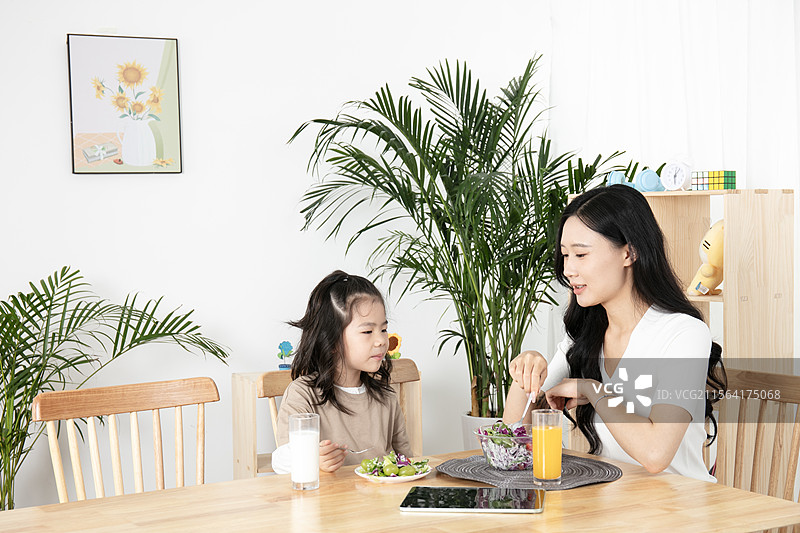 坐在桌边一起吃沙拉的年轻母女图片素材