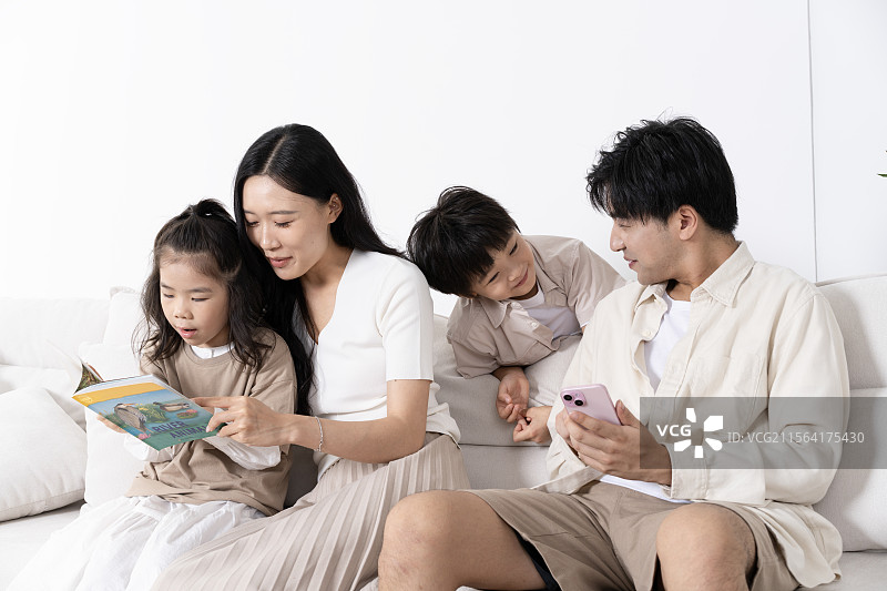 一家四口坐在沙发上看书与看手机图片素材