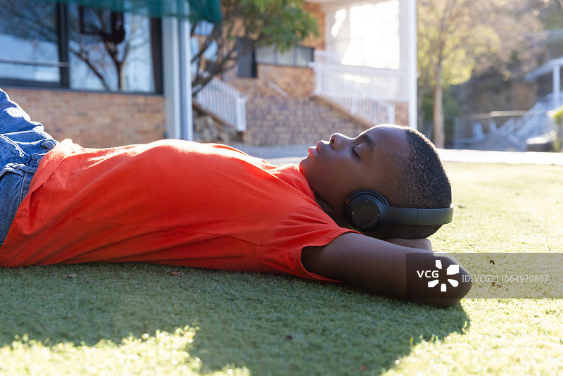 男孩在学校外的草地上戴着耳机放松，听音乐。图片素材