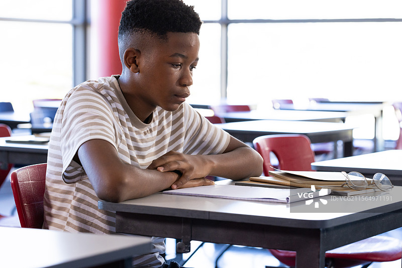 在学校，男孩坐在书桌前，专注地看着书和笔记本。图片素材