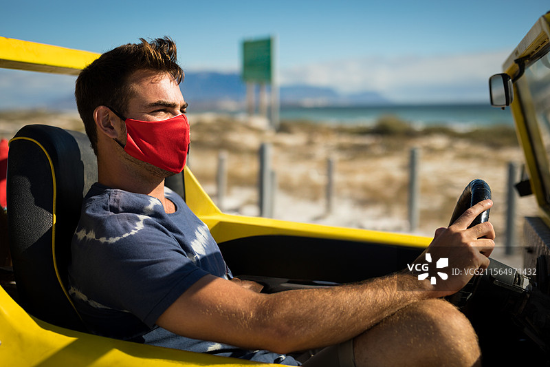 年轻男子驾驶着黄色敞篷车在海岸公路上，脸上戴着红色口罩图片素材