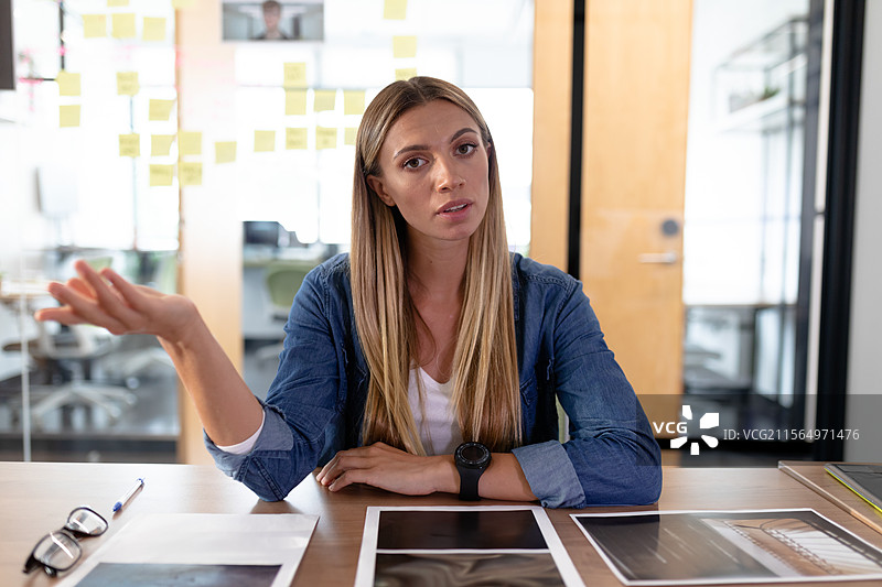 女性坐在现代办公室会议室，正在用平板电脑查看文件，佩戴眼镜并拿着笔。图片素材
