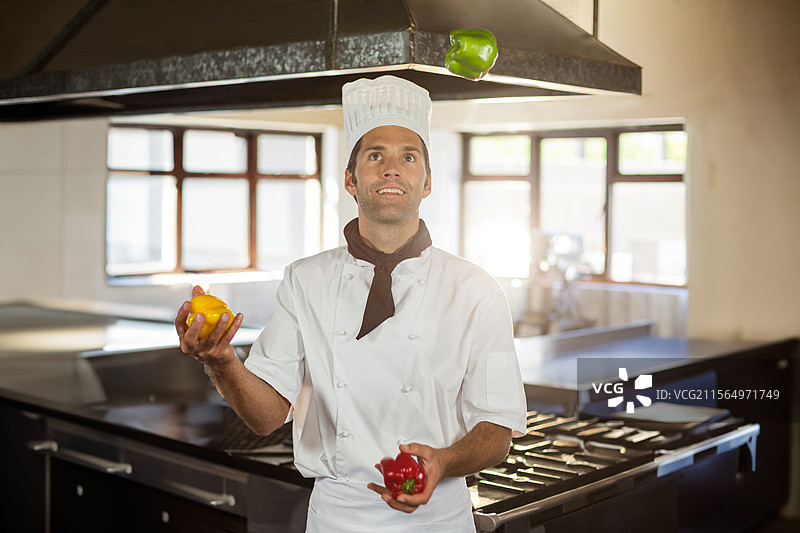 中年男性厨师在商业厨房中玩弄五彩椒，展示烹饪技巧图片素材