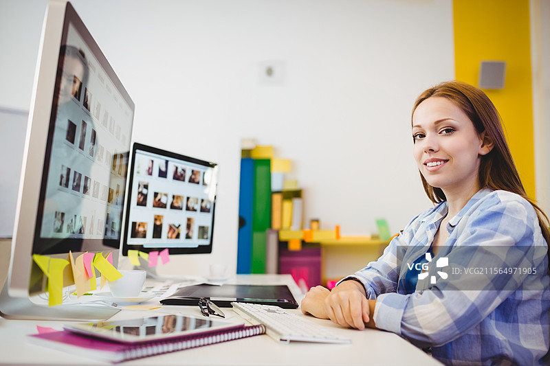 青少年女性坐在书桌前使用电脑，在家庭办公室里，配有显示器和平板，留有空白空间图片素材