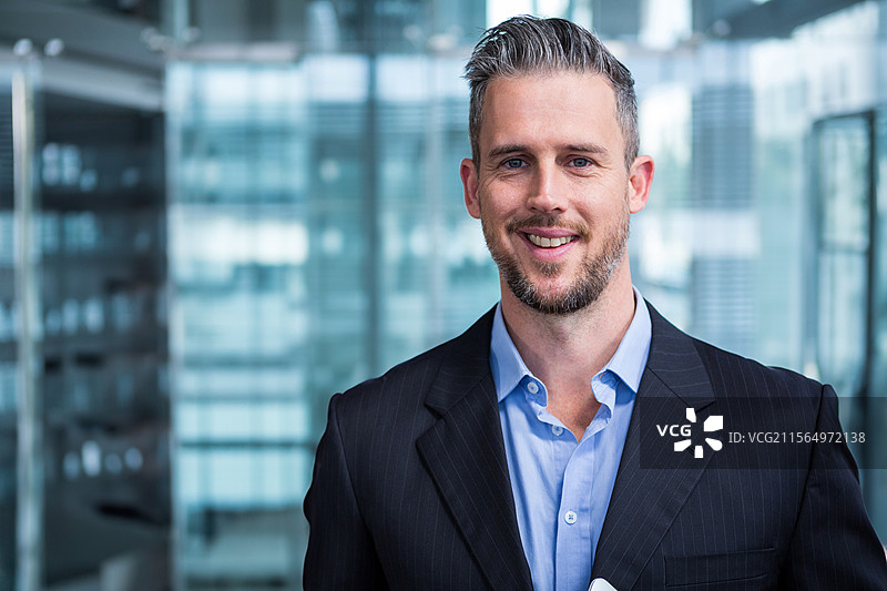 年轻男子在现代办公室里微笑着站着，玻璃墙旁有空白空间图片素材