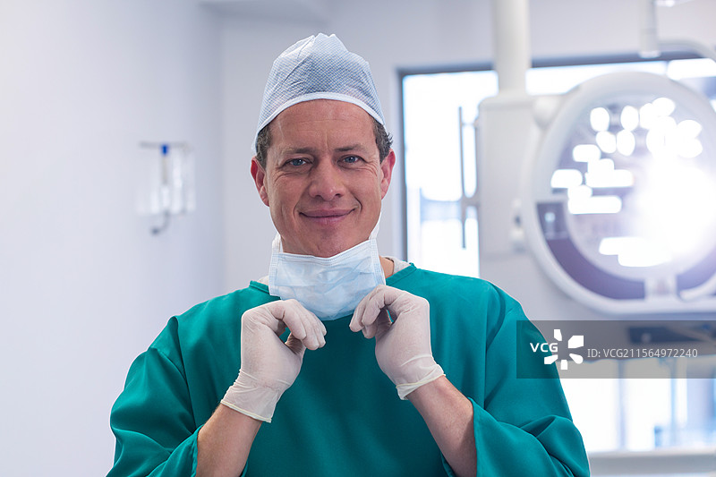 外科医生在手术室调整手术口罩，配有头顶灯和手套图片素材