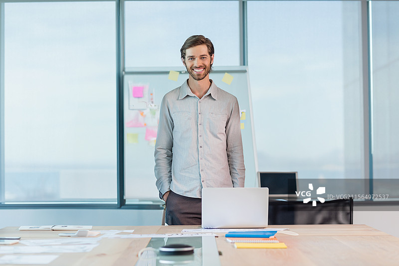 现代办公室中，男子站在会议桌后，展示翻转图表和笔记本电脑，留有空白空间。图片素材