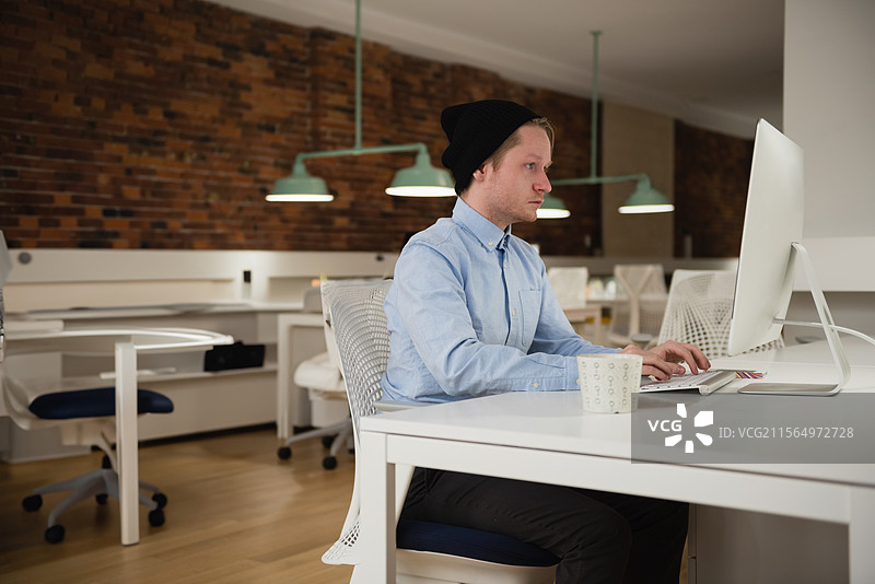 年轻男子在办公室桌子上打字，白色显示器和咖啡杯，留白空间图片素材