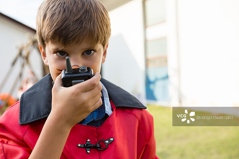 年轻男孩穿着红色夹克和蓝色衬衫，在后院用黑色对讲机说话，留有空白空间图片素材