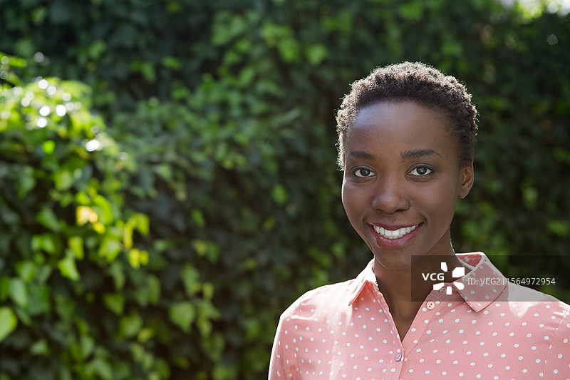 一位非裔美国女性站在常春藤墙前，穿着衬衫，面带微笑，留有空白空间。图片素材