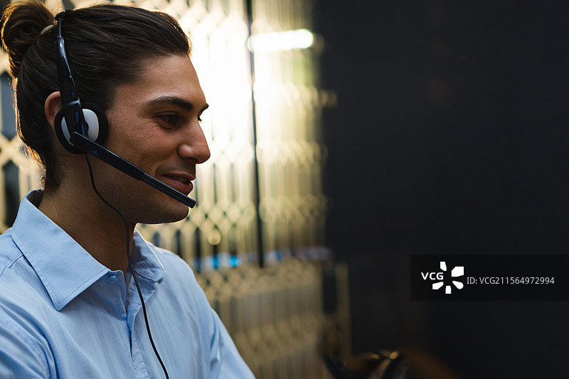 年轻男子在呼叫中心通过耳罩式耳机通话，背景有蜂窝隔断，留白空间图片素材
