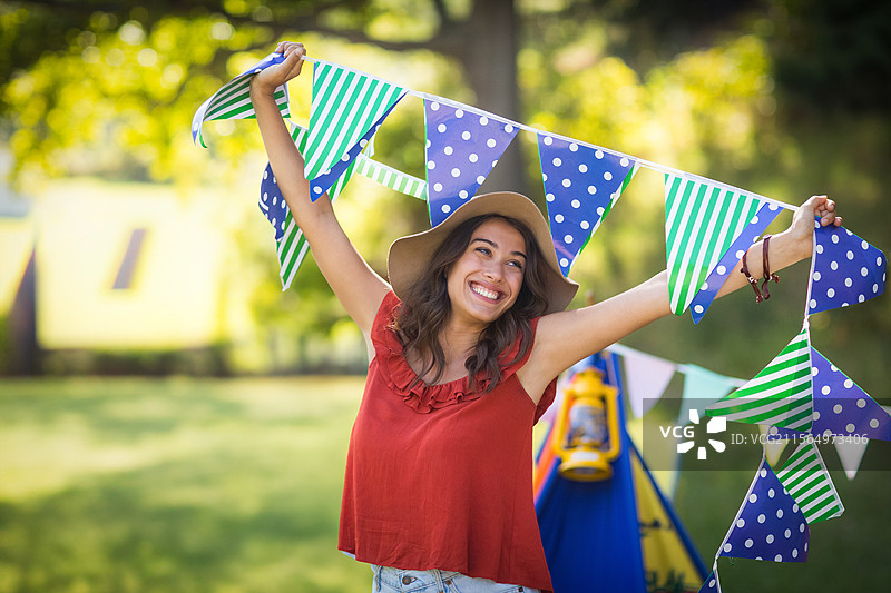 年轻女性在后院花园中举起三角旗，旁边有蓝色的游乐帐篷和黄色的灯笼。图片素材