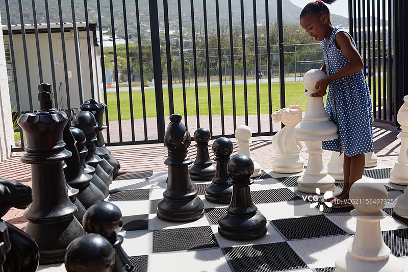 非裔美国儿童在棋盘露台上放置巨大的白色棋子，周围有棋子，留有空白空间图片素材