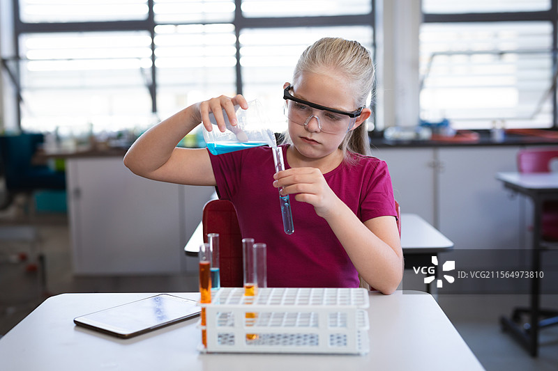 女孩在实验室桌子上将蓝色液体倒入试管，旁边有试管架和药片。图片素材