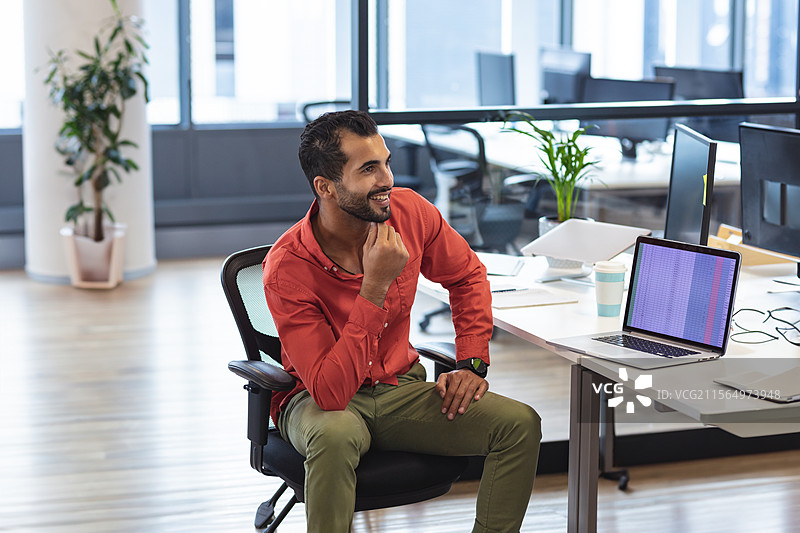 在现代开放式办公室的桌子上工作的人，使用笔记本电脑，旁边有咖啡、文件和眼镜。图片素材