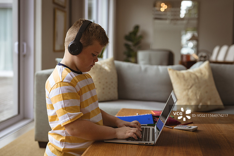 孩子在客厅靠近餐区的笔记本电脑上打字，戴着耳机，旁边有笔记本，留有空白空间图片素材