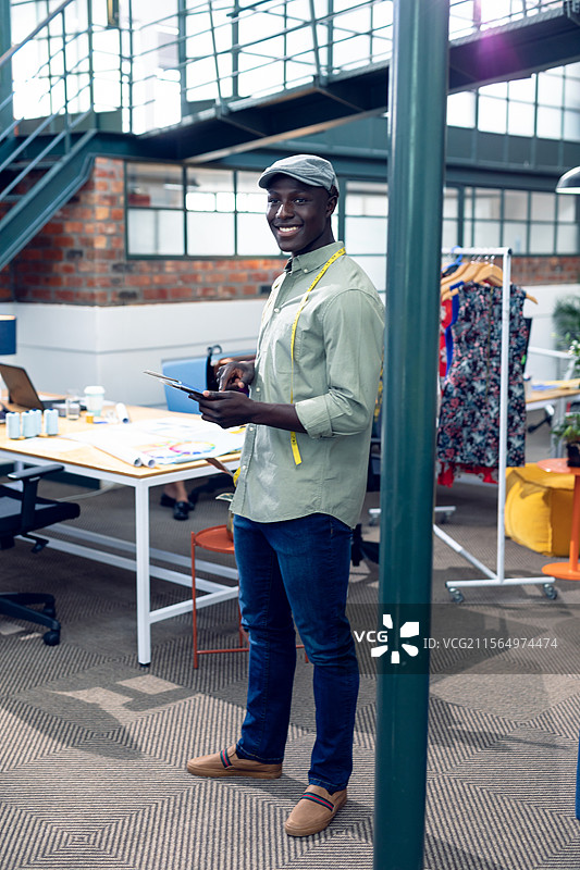 非裔美国男性在时尚工作室中使用数字平板电脑查看设计，并用卷尺测量。图片素材