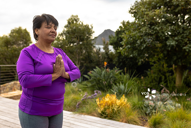 双种族老年女性在花园甲板上练习瑜伽，周围有栏杆和多肉植物，留白空间图片素材